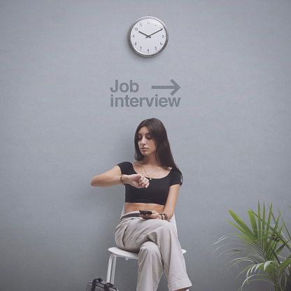 Young bored student sitting on a chair and waiting for a job interview, she is checking the time