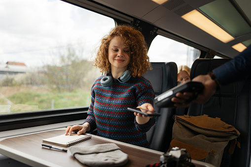 Smiling redhead woman using her mobile app while paying for a ticket in a train.