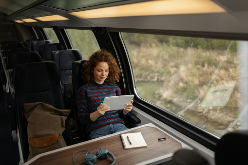 Young redhead woman reading her itinerary on touchpad while traveling by train.