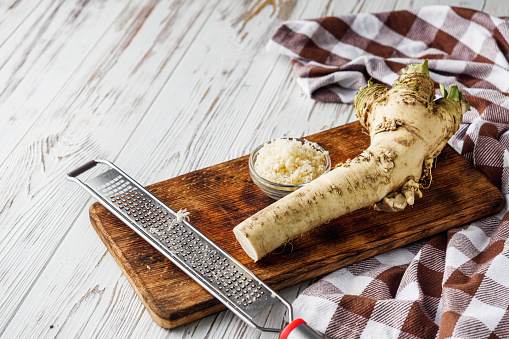 aromatic horseradish root on a white rustic wooden background.
