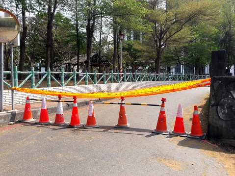 Close up of orange construction cones with yellow warning tape at road construction site in Taiwan before city road repair and reconstruction is blocked. Road closed sign and blurred background.
