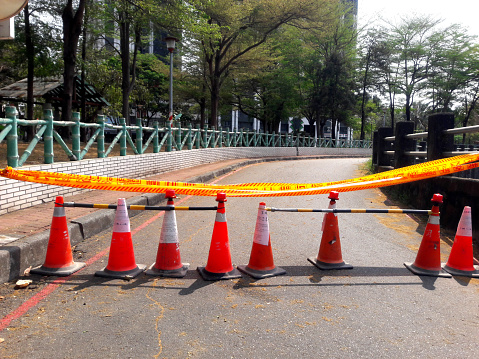 Close up of orange construction cones with yellow warning tape at road construction site in Taiwan before city road repair and reconstruction is blocked. Road closed sign and blurred background.