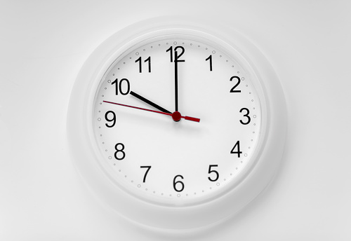 A Modern white wall clock with aluminium frame. Close up to a wall clock, the pointers at quarter pass 4. Selective focus on the number 5 or 5 o'clock. Reflections in the aluminum frame of the watch.
