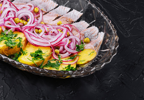 Sliced herring with baked potatoes and marinated onions on glass plate