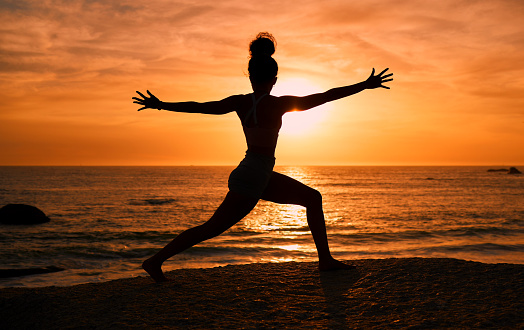 Meditation, yoga and silhouette of woman on beach at sunrise for exercise, training and pilates workout. Morning, fitness and shadow of girl balance by ocean for sports, body wellness and stretching