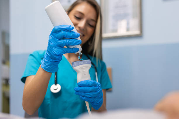 femme médecin souriante appliquant du gel sur un appareil à ultrasons avant le traitement. les mains dans les gants appliquent une bande de gel transparent sur le capteur du scanner à ultrasons. - gynecologist ultrasound human pregnancy gynecological examination photos et images de collection