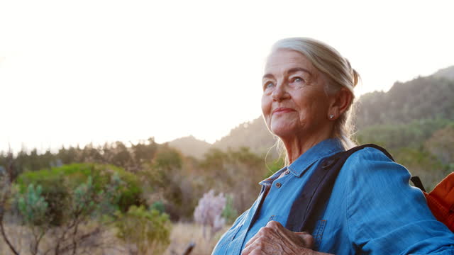 Close Up Portrait Of Active Senior Woman With Backpack Hiking In Countryside