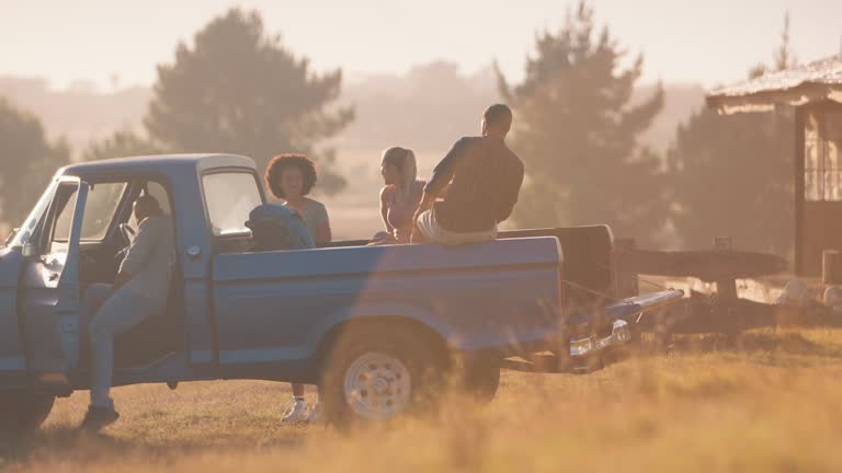 Group of friends loading backpacks onto pick up truck on road trip to cabin in countryside at sunset - shot in slow motion