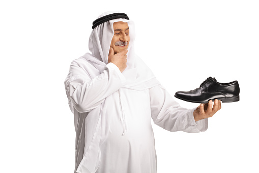 Arab man holding a black leather shoe and thinking isolated on white background
