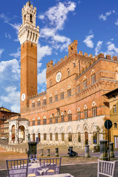 A view of the Palazzo Pubblico in the Piazza del Campo in the medieval heart of Siena in Tuscany A suggestive view of the majestic Torre del Mangia (Mangia tower) and the Palazzo Pubblico in the Piazza del Campo, in the medieval heart of Siena, in Tuscany. Built in 1290 as the seat of the Council of Nine and of the executive power of the city, the majestic Palazzo Pubblico is still the seat of the municipal government. The Torre del Mangia was built between 1338 and 1348 on a project by Giovanni Balduccio, known as Mangia, becoming the symbol of the political and military power of Siena compared to its rival Florence. Center of the city life since 1169, Piazza del Campo or simply Campo is one of the most beautiful and famous squares in the world for its particular shell shape. In this space every year the seventeen historical neighborhoods of Siena compete in the Palio, one of the oldest horse races in the world. Siena is one of the most beautiful Italian cities of art, in the heart of the Tuscan hills, visited for its immense artistic and historical heritage and for its famous popular traditions. Since 1995 the historic center of Siena has been declared a World Heritage Site by UNESCO. Wide angle image in High Definition quality. torre del mangia stock pictures, royalty-free photos & images