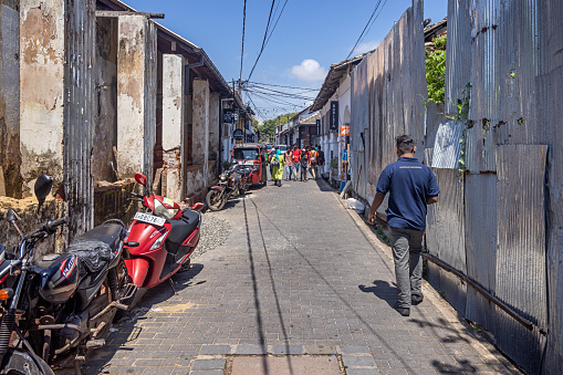 Galle, Sri Lanka - February 11th 2023:  Man walking down a narrow street in front of a wall made of corrugated iron Galle, the most southern city on Sri Lanka