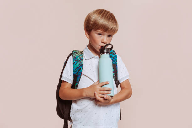 un écolier avec sac à dos boit une bouteille d’eau - water child bottle little boys photos et images de collection