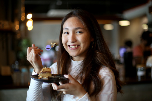 Portrait of an Asian young woman enjoying cake in café