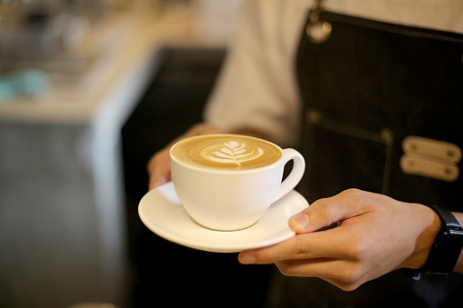 An Asian young man is holding a cup of freshly made flat white coffee in café