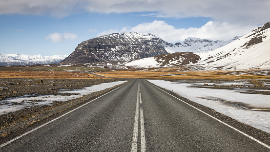 Icelandic Empty Road 1 Ring Road Panorama. Famous Roadtrip Route 1 in Wintertime with snowcapped mountain range in the background under sunny blue skyscape. Route 1, Southern Iceland in Winter, Nordic Countries, Northern Europe.