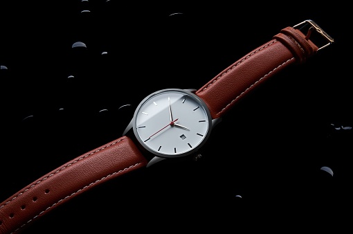 A close-up shot of a classic-style wristwatch with a brown leather band, on a wet and dark surface.