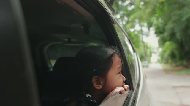 Asian little girl sitting in the car and looking out of the window