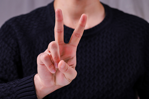 Young man holding two fingers up showing peacekeeping struggle or victory symbol and letter V in sign language.