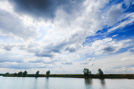 Beautiful view on blue sky and white clouds above the river, tree grove on the riverbank