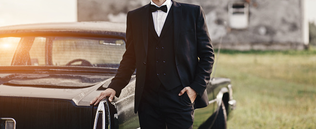 Confident wealthy elegant man in suit near classic car