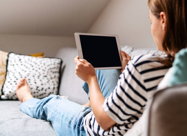 istock Woman holding tablet in her hands and looking at screen while lying on sofa. 1481354260