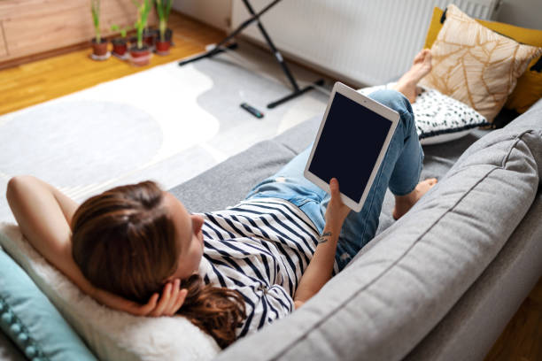 istock Woman lying down on sofa at home and reeding ebook. 1481354294