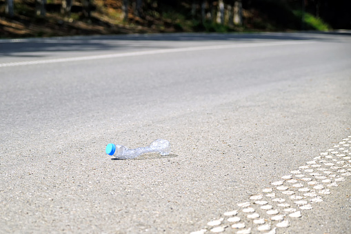 An empty plastic water bottle was thrown out onto a country road against the backdrop of a forest. Problems of ecology and environmental protection.