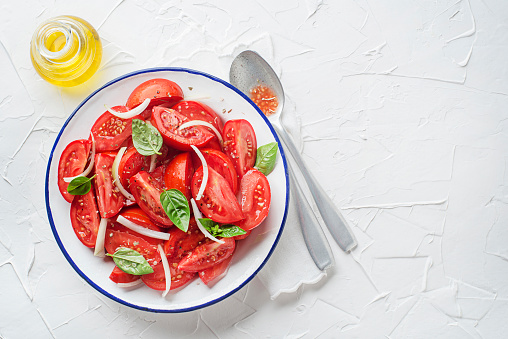 Fresh tomato salad with onion and basil on white table background. Concept for a tasty and healthy meal