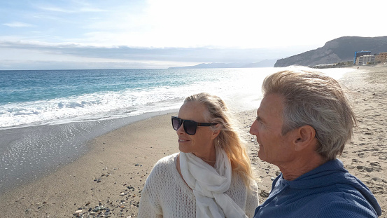 Senior couple walk along beach at seaside