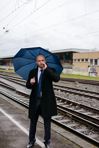 Man in suit and coat standing in the rain outside the train station