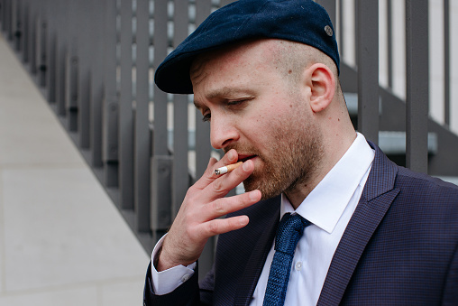 Portrait of a man in a blue suit and cap looking away and smoking a cigarette