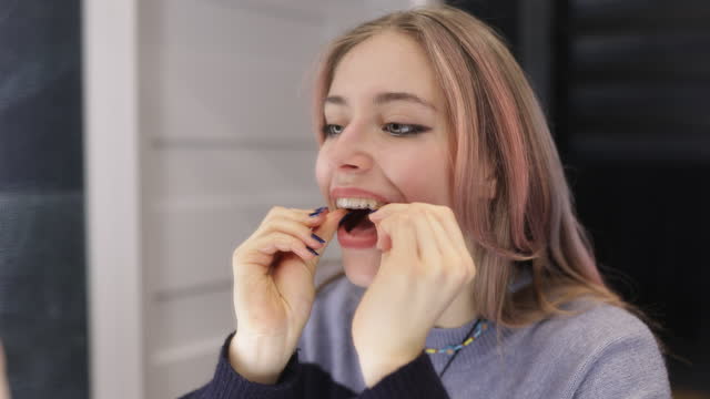 Teenage girl is putting on her transparent dental aligner in the bathroom