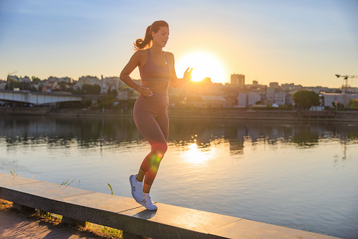 Woman in sports clothes jogging on platform by the city river at dawn, fit women working out
