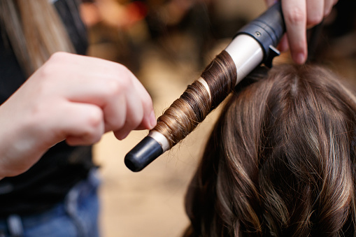 Using hot curler and making curls on brunette customer's hair strands, new hairstyle