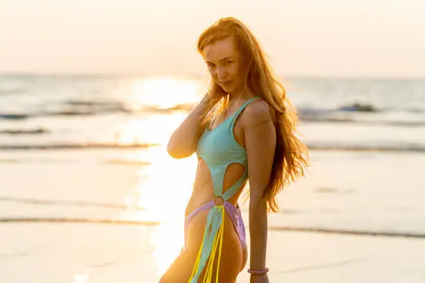 Photo of Beautiful caucasian woman in bikini at the beach during a beautiful sunset moment. Nice sun lights and rays from the sea