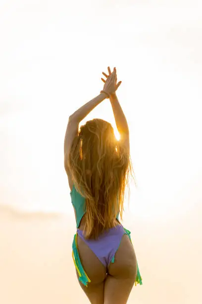 Photo of Sexy back view of a beautiful caucasian woman with curvy body shape in bikini at the beach looking at the beautiful sunset moment