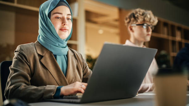 istock Group of Diverse Young Creative Colleagues Sitting Next to Each other and Working On Laptops in Modern Office. Muslim Woman Smiling After Successfully Finishing a Task. Office Team Work 1481369201