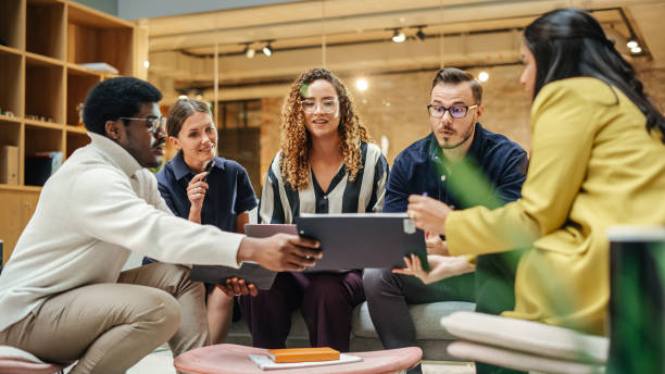 istock Multiethnic Group of Creative People Working on Project in a Modern Bright Office. A Diverse Group of Colleagues Developing a New Approach Using Charts, Laptop, and Tablet. Wide Shot 1481369393