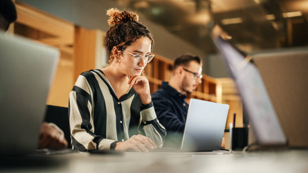 portrait of enthusiastic hispanic young woman working on computer in a modern bright office. confident human resources agent smiling happily while collaborating online with colleagues. - arbeta bildbanksfoton och bilder