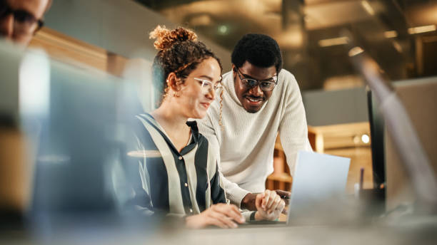 istock Portrait of Two Creative Colleagues Using Laptop to Discuss Work Project at Office. Young Black Technical Support Specialist Helping Female Customer Relationship Coordinator. Teamwork Concept 1481370596