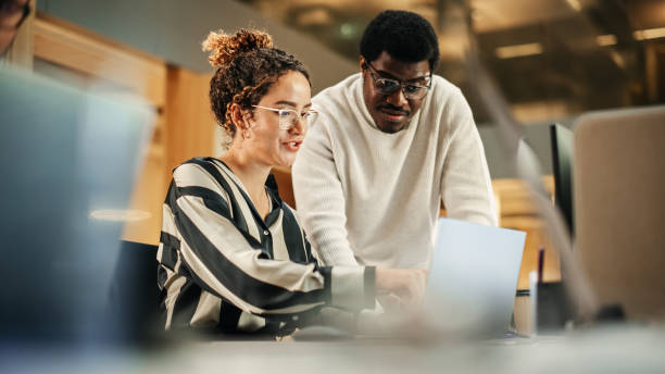 istock Portrait of Two Creative Colleagues Using Laptop to Discuss Work Project at Office. Young Black Technical Support Specialist Helping Female Customer Relationship Coordinator. Teamwork Concept 1481370629