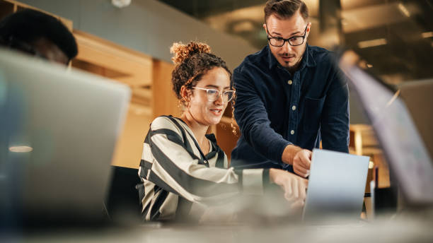 istock Two Colleagues Working On Laptop in Office. Female Hispanic Help Desk Coordinator Collaborates with White Male Customer Service Agent, They Discuss a Project, Chat, Smile. Teamwork Collaboration 1481370752