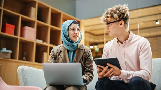 istock Two Young Creative Colleagues Discussing Work Project and Pointing at the Laptop screen in Office. Caucasian Male Supervisor Uses a Tablet and Consults Muslim Female Team Leader. 1481370838