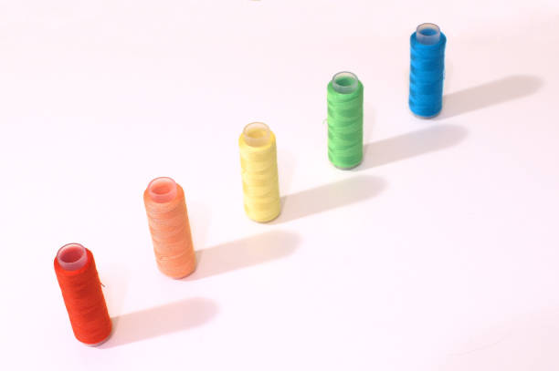 istock Spools of thread stacked in a diagonal line atop a white surface. 1481371611