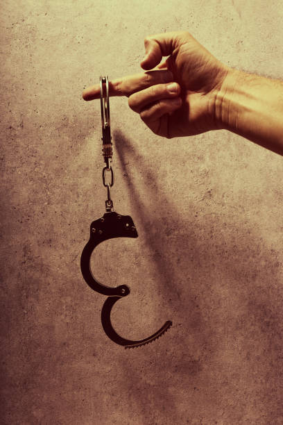 istock Hand holding handcuffs in front of a concrete background 1481371689