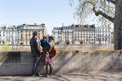 Couple and their little daughter looking at beautiful buildings around Seine riverbank.