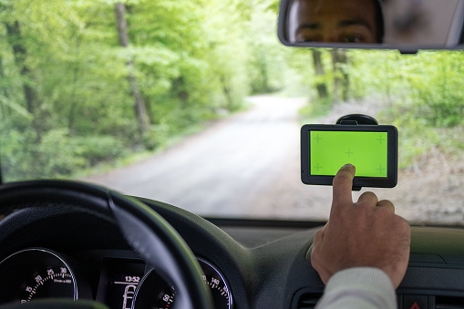 Close-up of man hands using digital tablet with green screen in center of windshield while driving car on road.