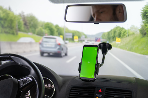 Close-up of smart phone with green screen in center of car windshield.