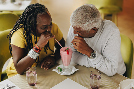 Mature couple sharing a delicious strawberry milkshake in a cafe. Carefree senior couple having a good time in a restaurant. Happy mature couple enjoying their retirement together.