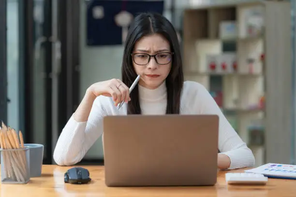 Photo of Concerned female worker looking at laptop screen suspiciously, thinking about problem-solving, reading ambiguous emails or negative news. Concept of focus and concentration